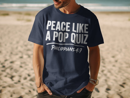 Navy t-shirt with white text "PEACE LIKE A POP QUIZ PHILIPPIANS 4:7" on a beach.