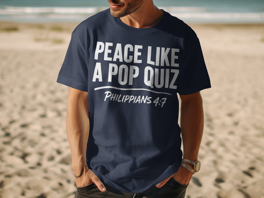 Navy t-shirt with white text "PEACE LIKE A POP QUIZ PHILIPPIANS 4:7" on a beach.