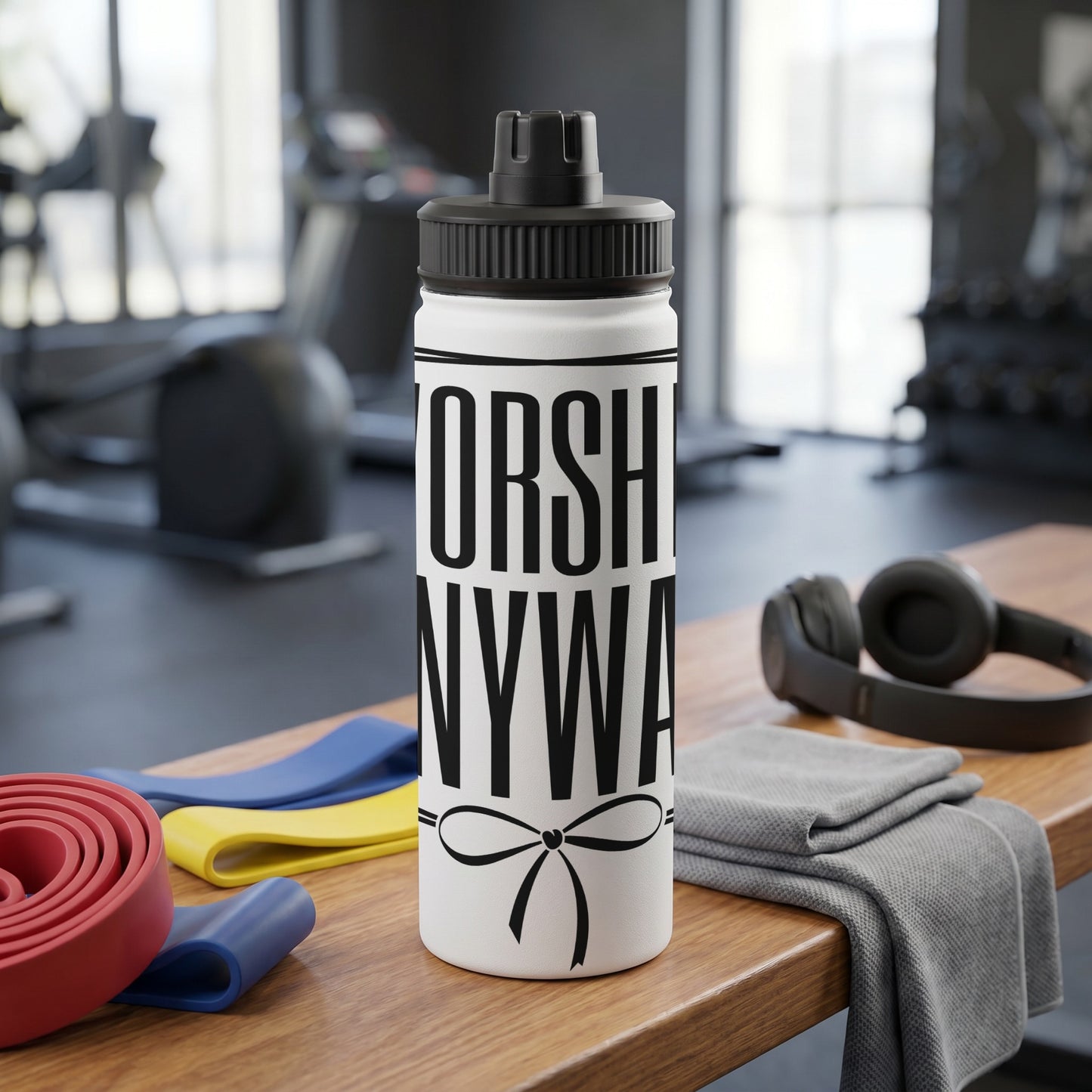 White water bottle with black text "WORSHIP ANYWAY" and a bow on a wooden table with resistance bands.