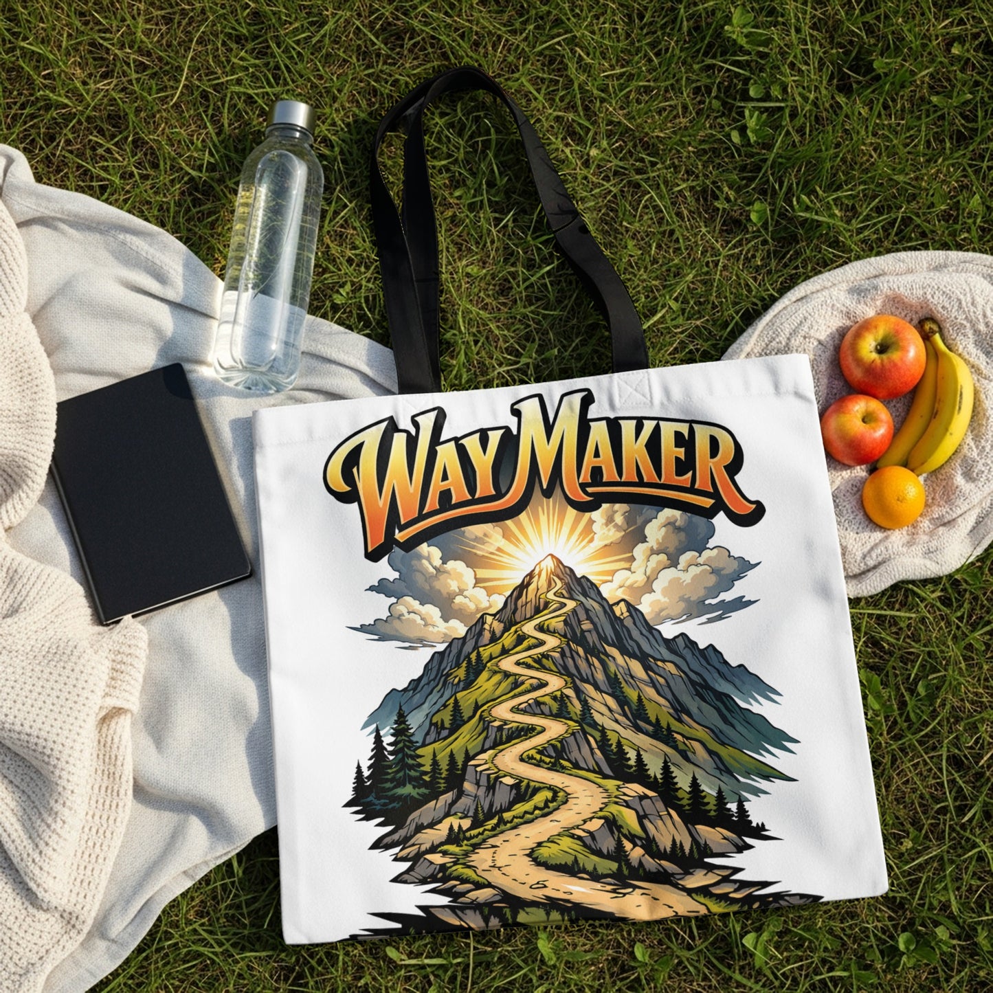 White tote bag with "Way Maker" text over a winding mountain path artwork.