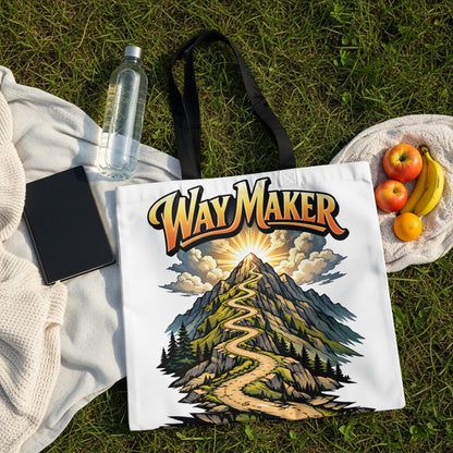 White tote bag with "Way Maker" text over a winding mountain path artwork.