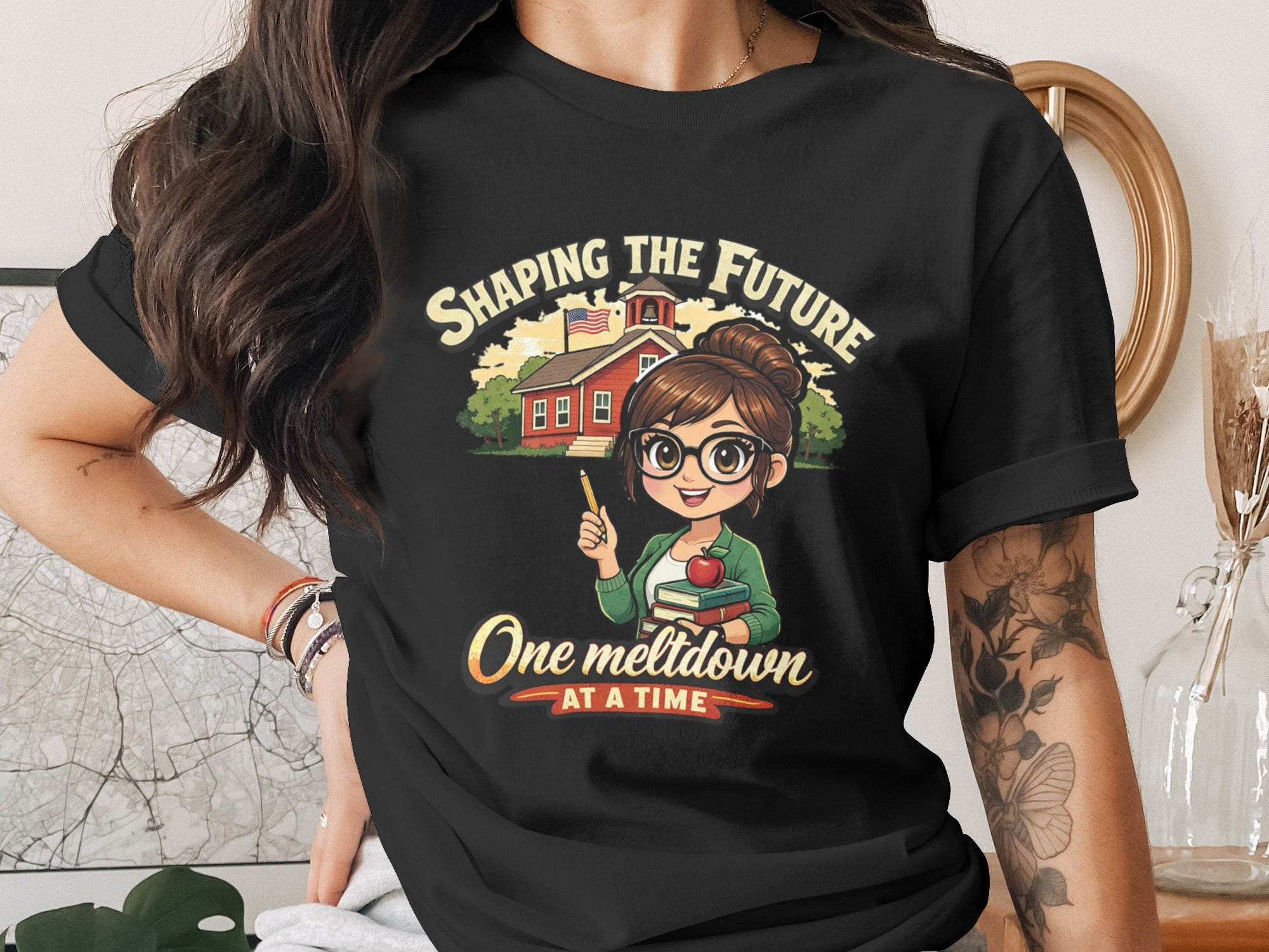 Teacher graphic on black shirt with text "SHAPING THE FUTURE One meltdown AT A TIME".