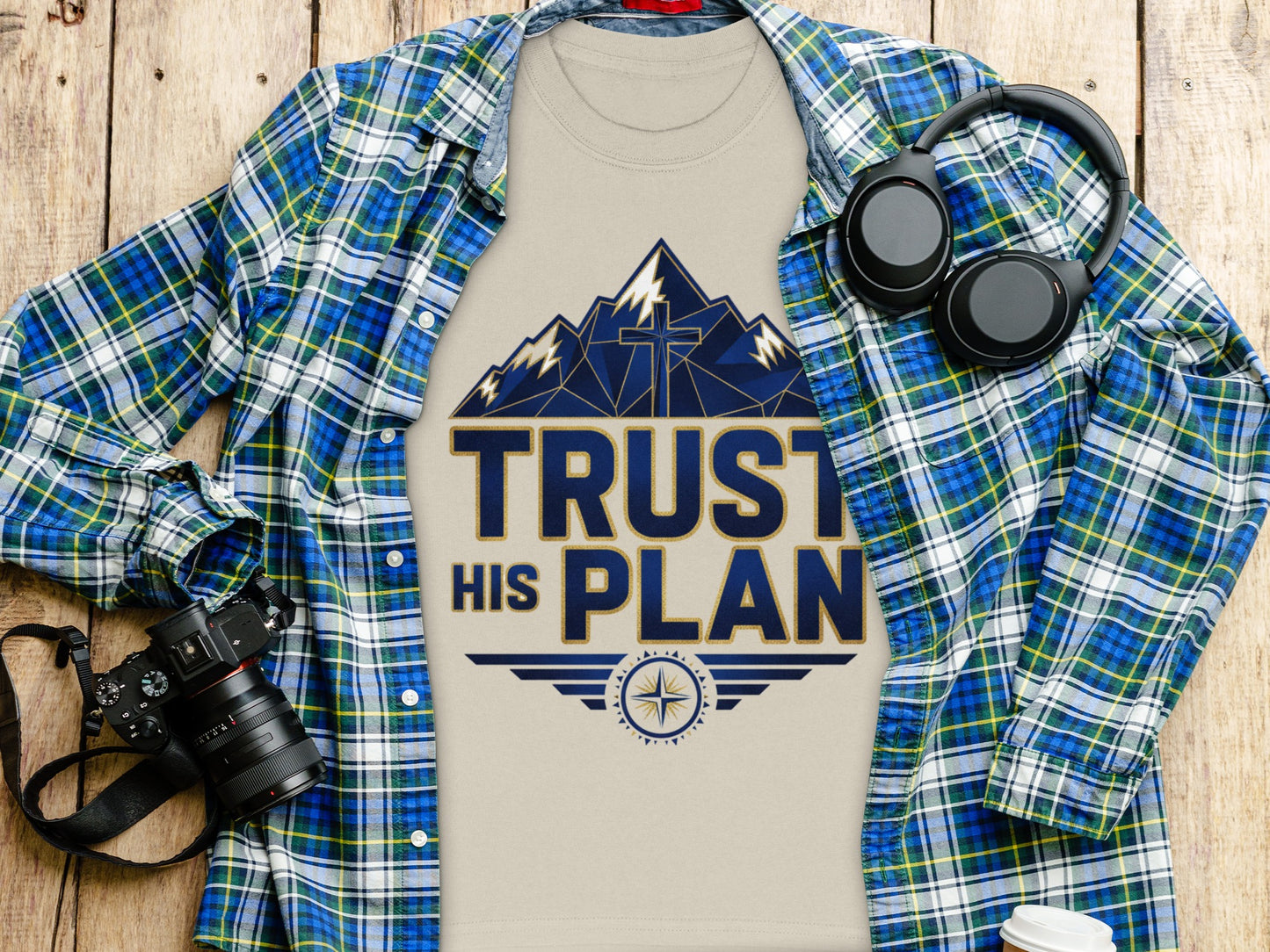 T-shirt with "TRUST HIS PLAN" text design, mountains, and cross, over plaid shirt.