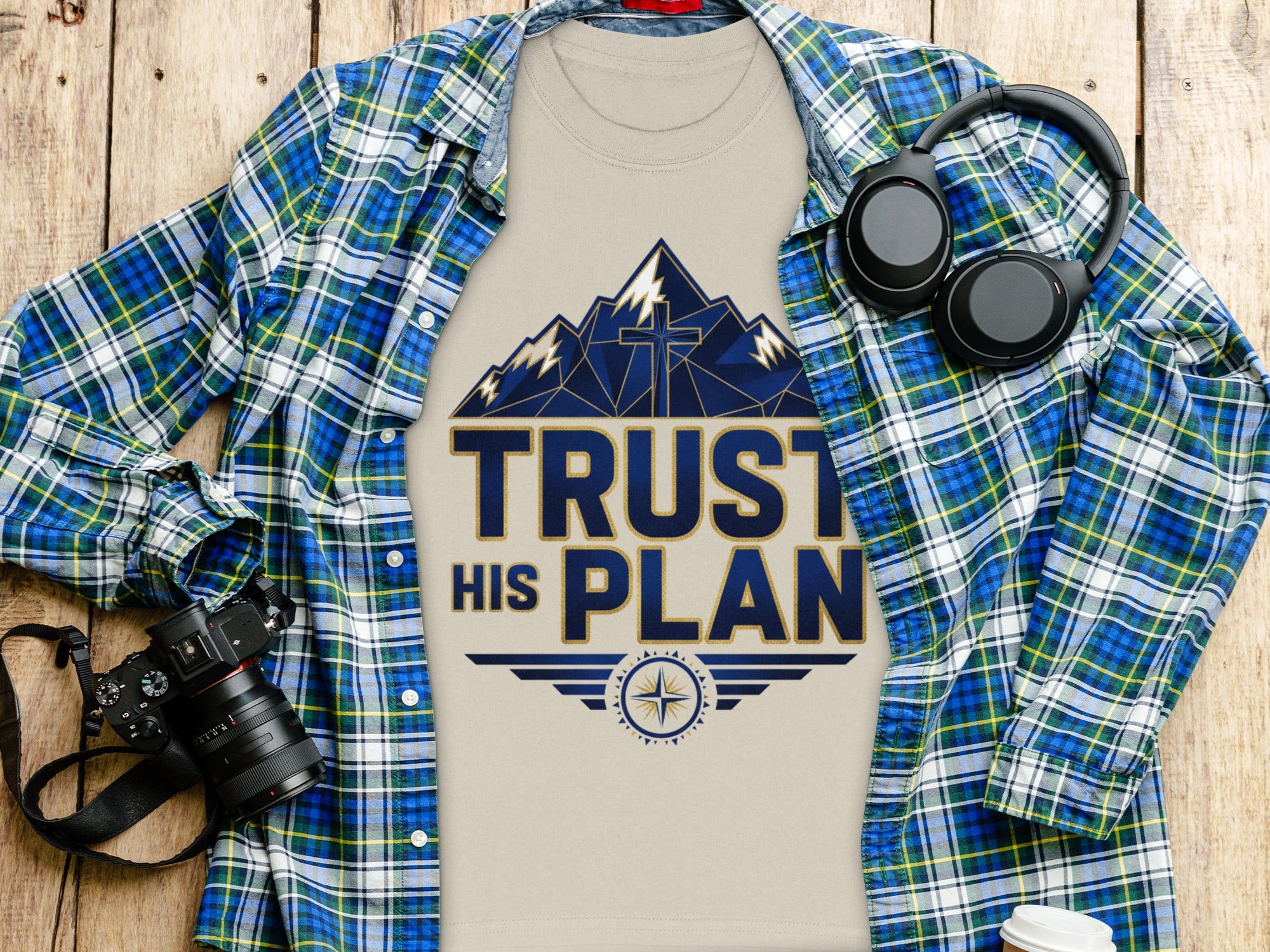 T-shirt with "TRUST HIS PLAN" text design, mountains, and cross, over plaid shirt.