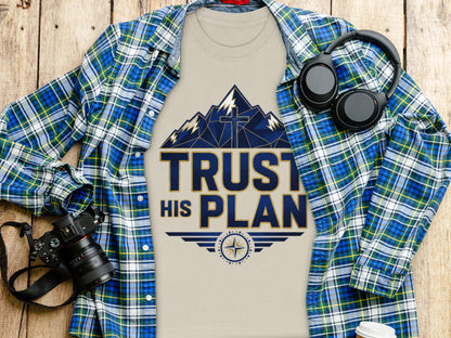 T-shirt with "TRUST HIS PLAN" text design, mountains, and cross, over plaid shirt.