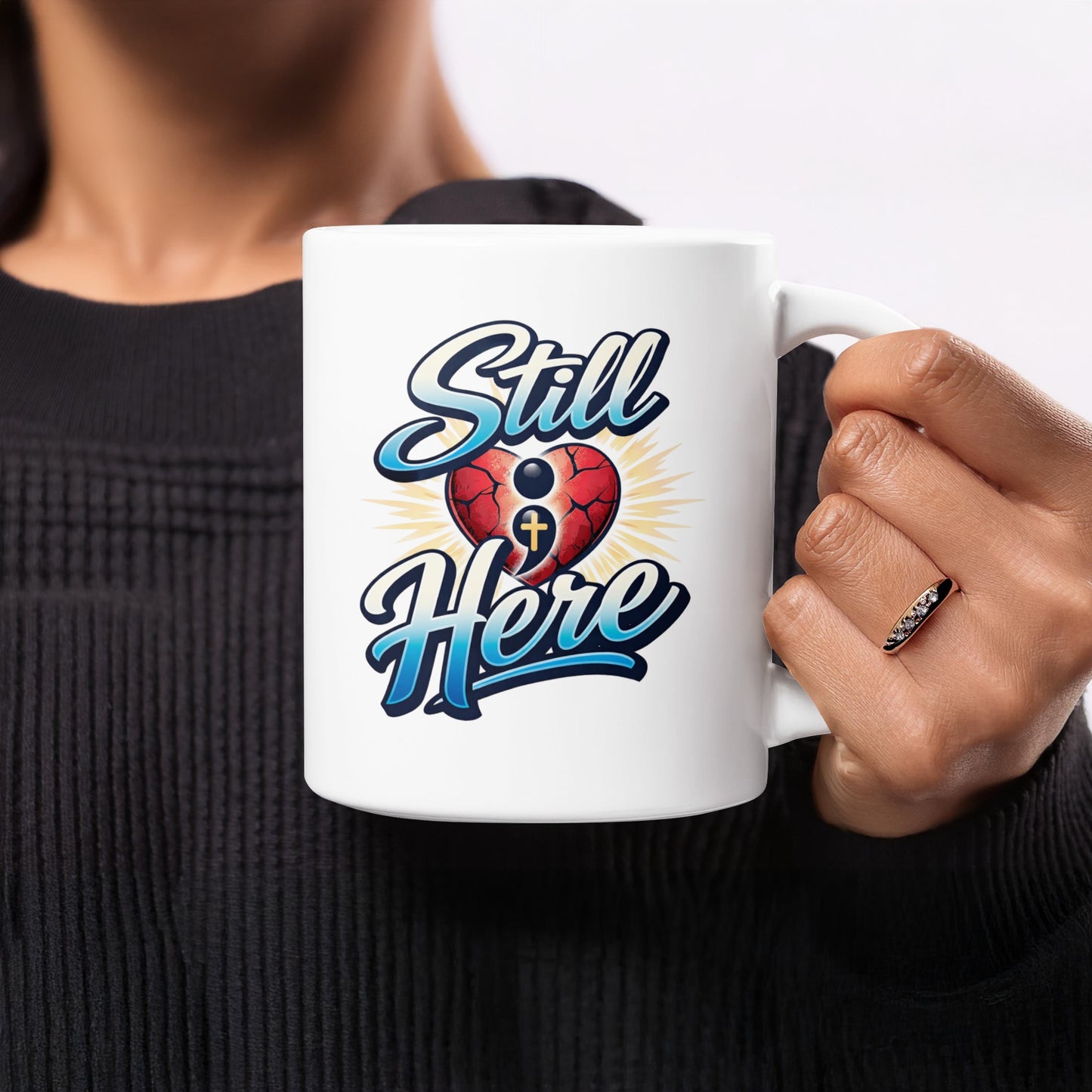 White mug with "Still Here" text, cracked heart, and cross graphic.