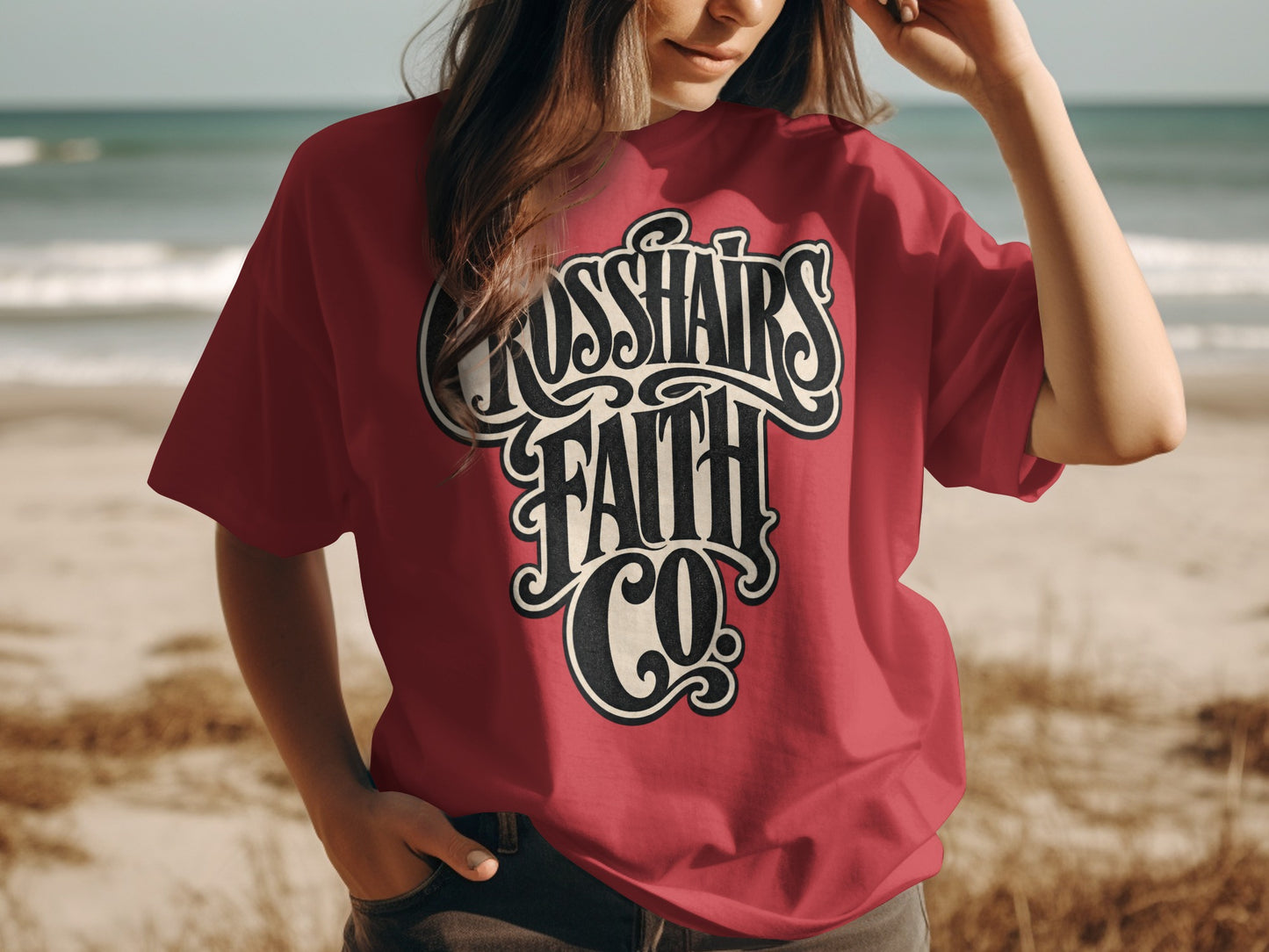 Red t-shirt with "Crosshairs Faith Co." logo on a beach.