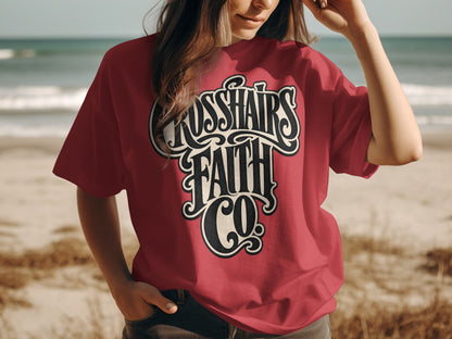 Red t-shirt with "Crosshairs Faith Co." logo on a beach.
