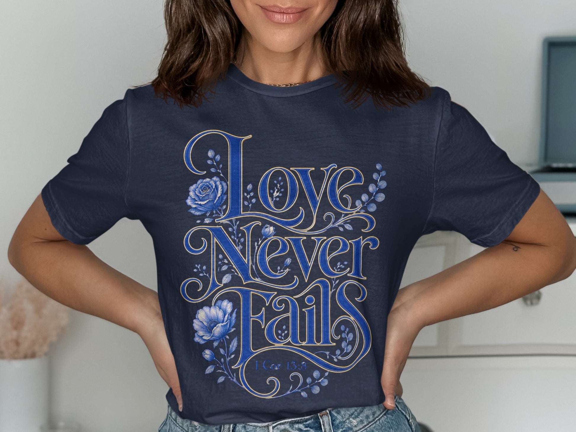 Navy t-shirt with "Love Never Fails" and 1 Cor 13:8 text, surrounded by blue floral accents.