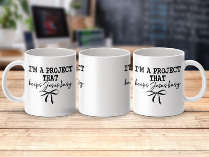 Three white mugs with "I'm a project that keeps Jesus busy" text and bow.