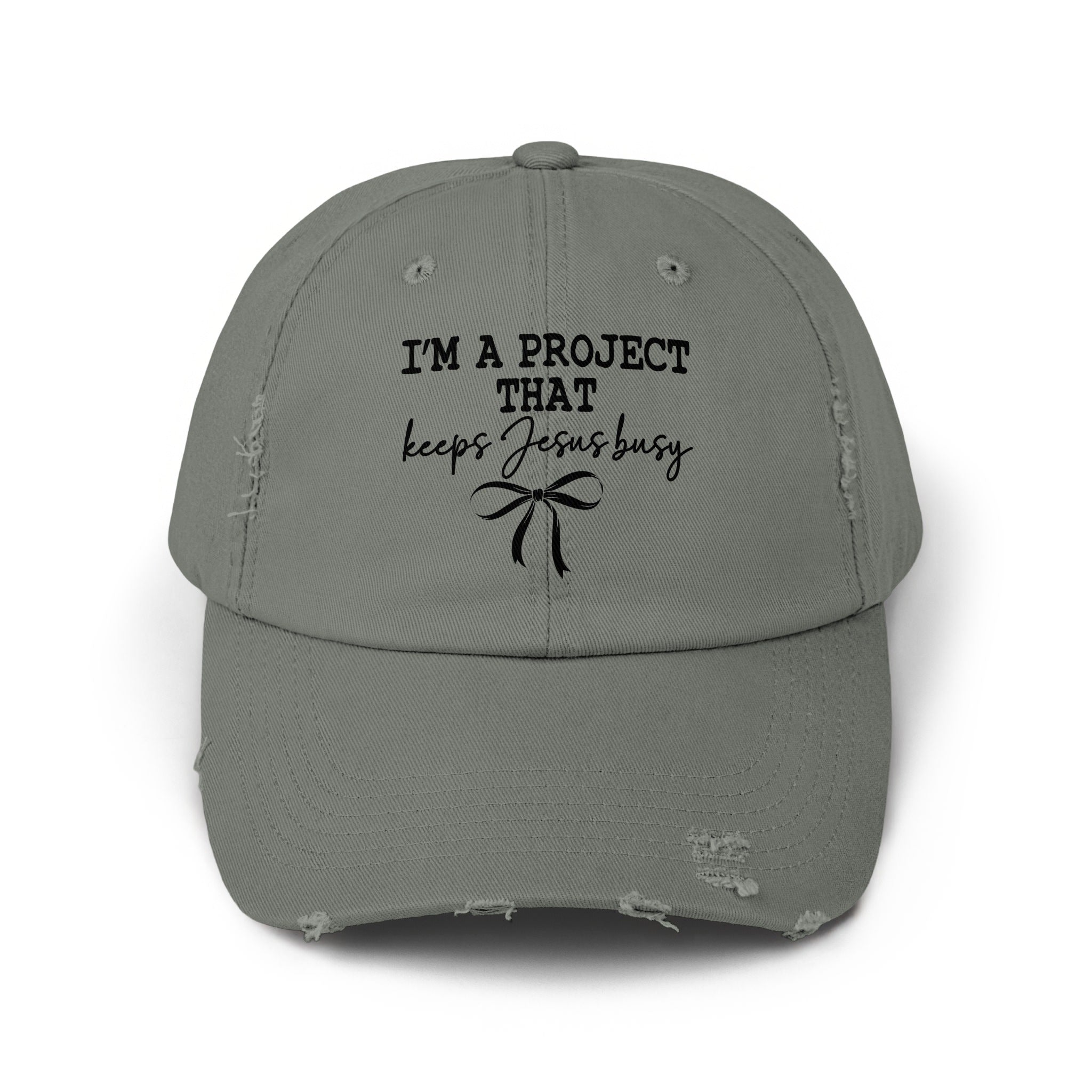 Distressed gray baseball cap with black text that reads "I'M A PROJECT THAT keeps Jesus busy" and a bow.