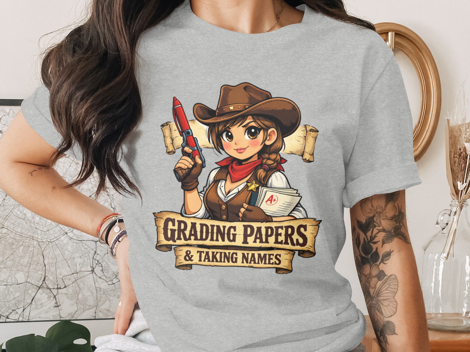 T-shirt graphic of a cartoon cowgirl holding a pen and papers with text "GRADING PAPERS & TAKING NAMES".
