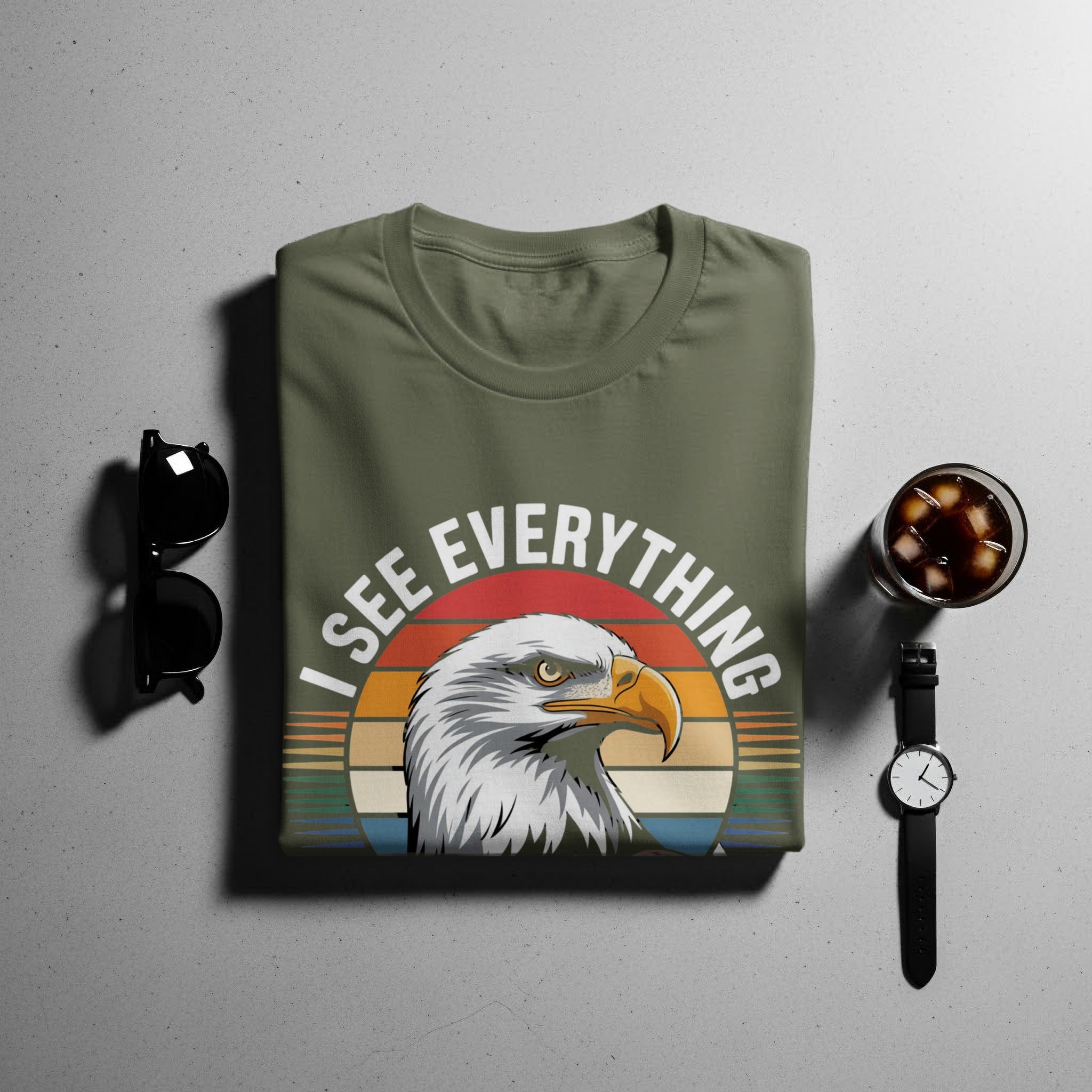 Olive green t-shirt with eagle graphic and text "I SEE EVERYTHING".