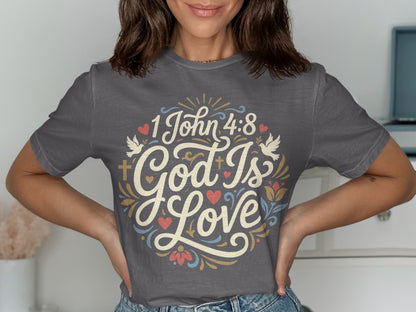 "1 John 4:8 God Is Love" text with doves, hearts, and floral design on a gray t-shirt.