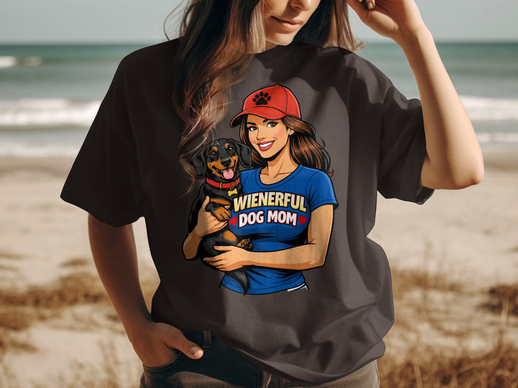 Woman in dark t-shirt holding dachshund, wearing red hat with paw print and blue shirt reading "WIENERFUL DOG MOM".