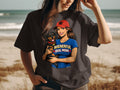Woman in dark t-shirt holding dachshund, wearing red hat with paw print and blue shirt reading "WIENERFUL DOG MOM".