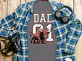 Grey t-shirt with "DAD 01" text and bull graphic, overlaid by plaid shirt.