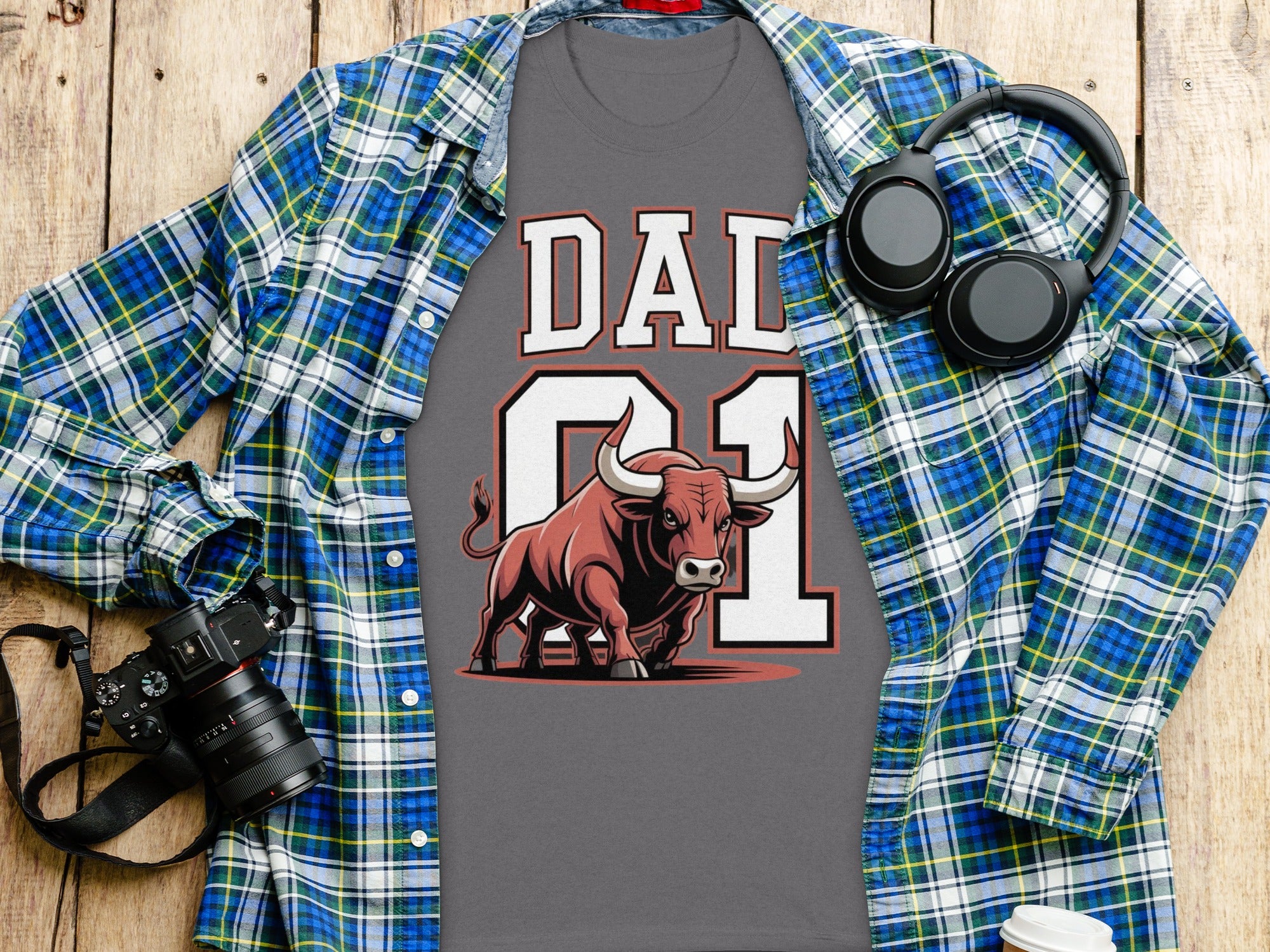 Grey t-shirt with "DAD 01" text and bull graphic, overlaid by plaid shirt.