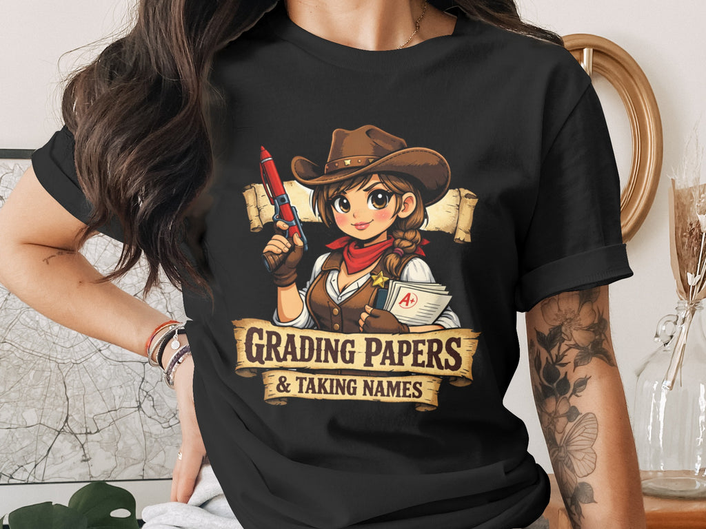 Cowgirl character with a red pen and papers on a black t-shirt with "Grading Papers & Taking Names" text.
