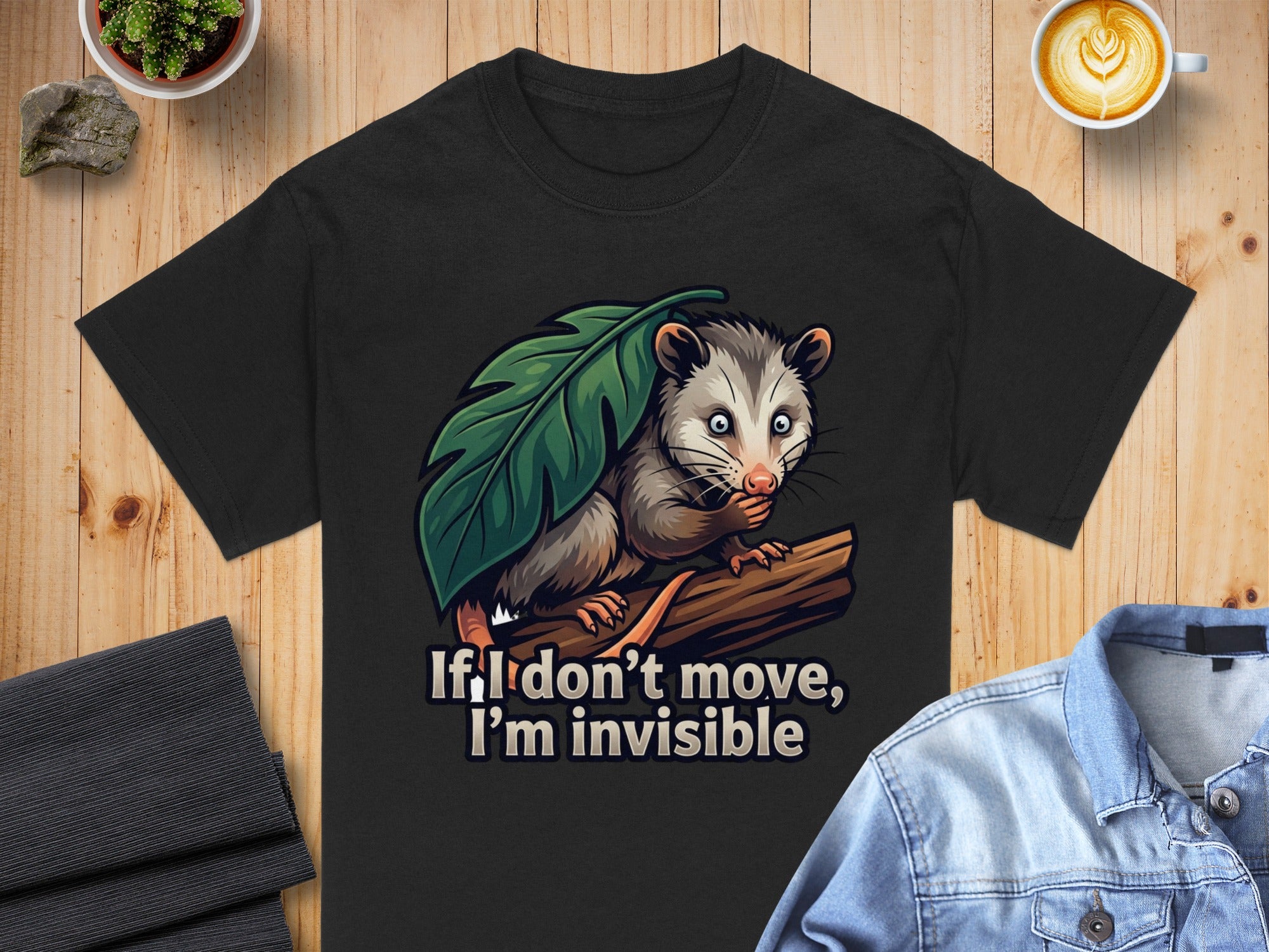Black t-shirt with a possum hiding behind a leaf, text says: If I don't move, I'm invisible.