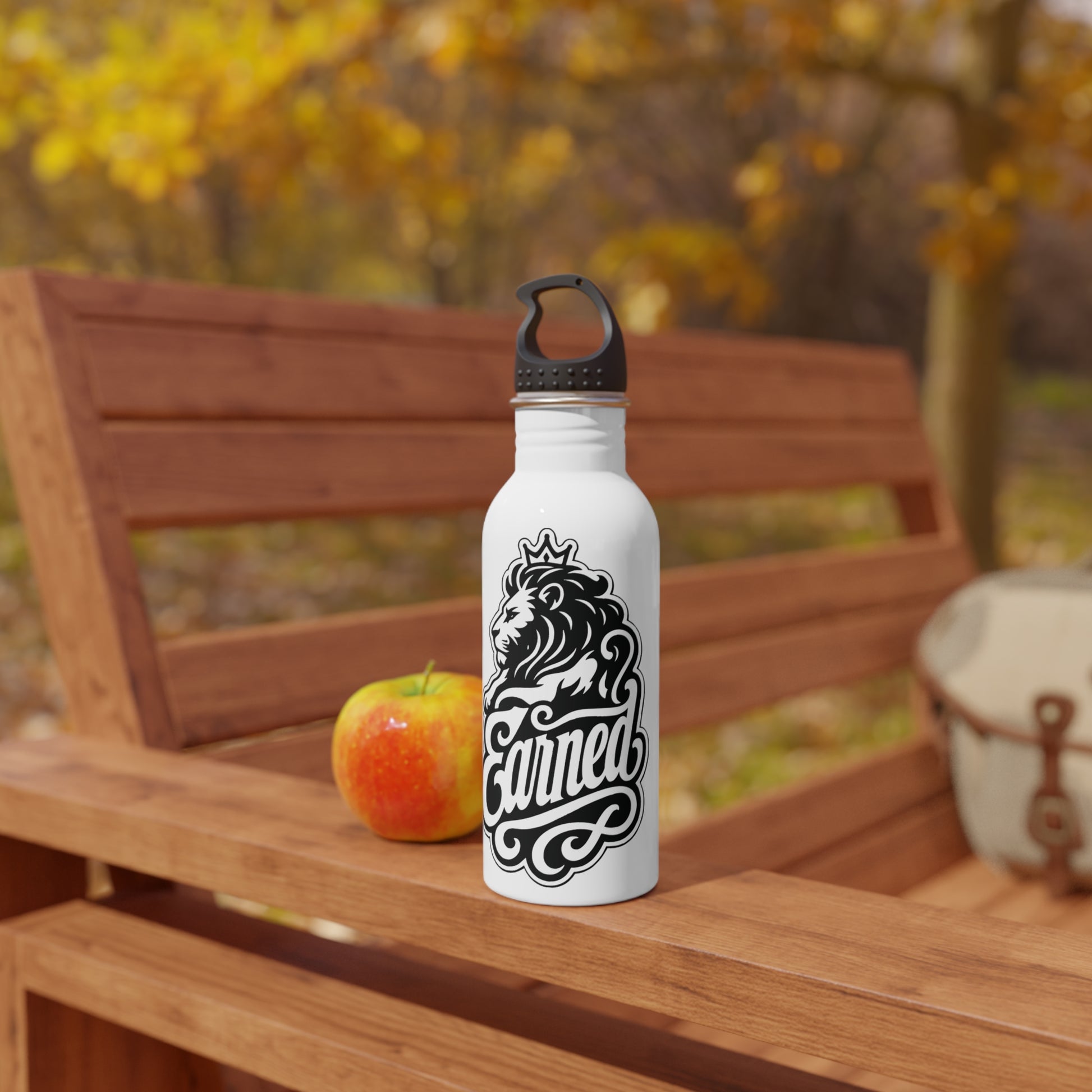 White water bottle with lion and "Earned" text on wooden bench with apple.