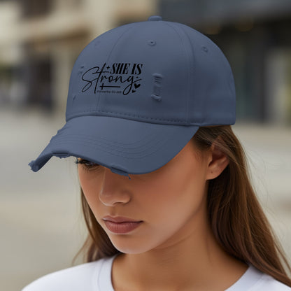 Distressed navy baseball cap with "SHE IS Strong" and Proverbs 31:25 text.