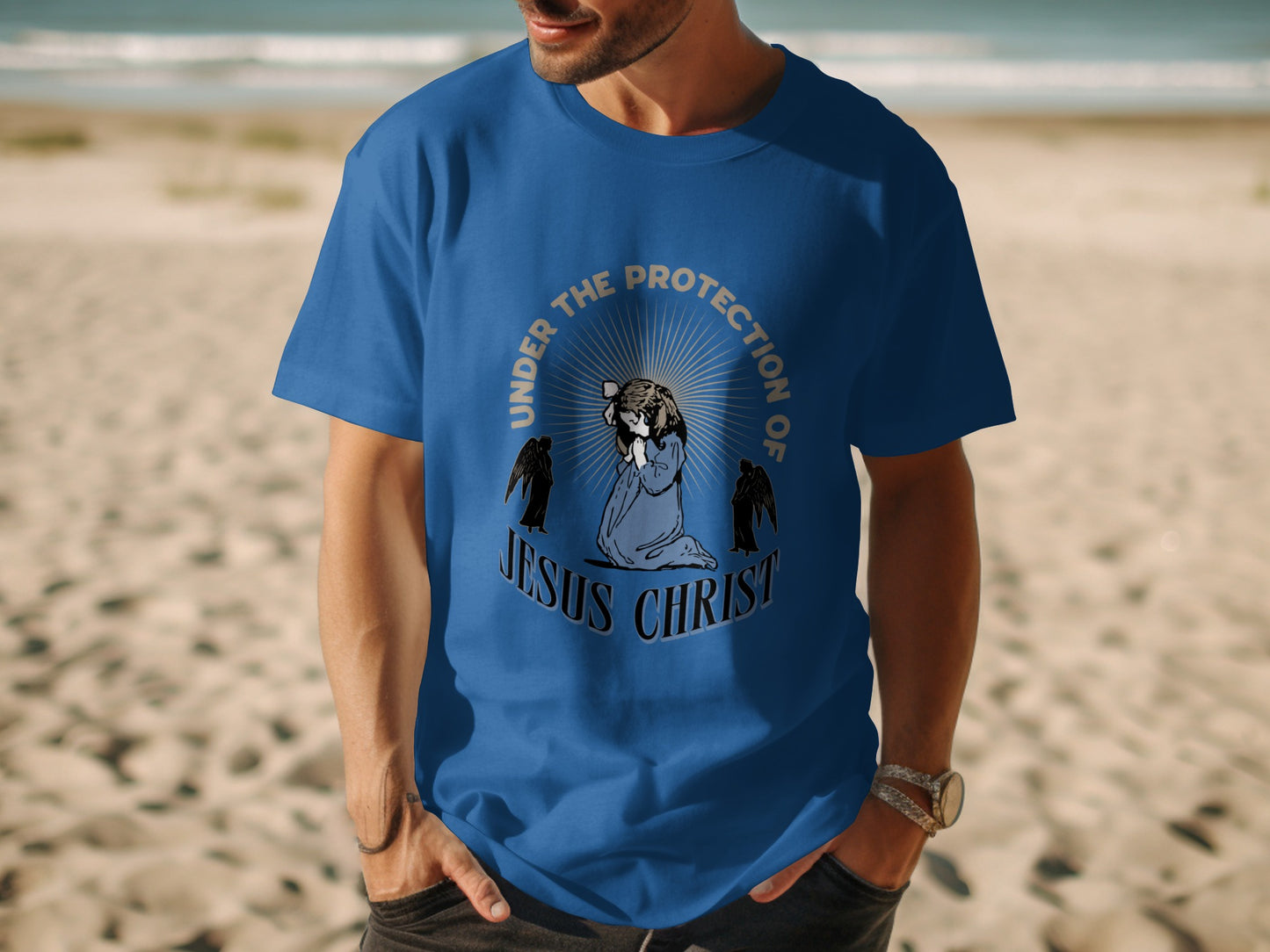 Blue t-shirt with graphic of praying figure, wings, and text "Under the Protection of Jesus Christ".