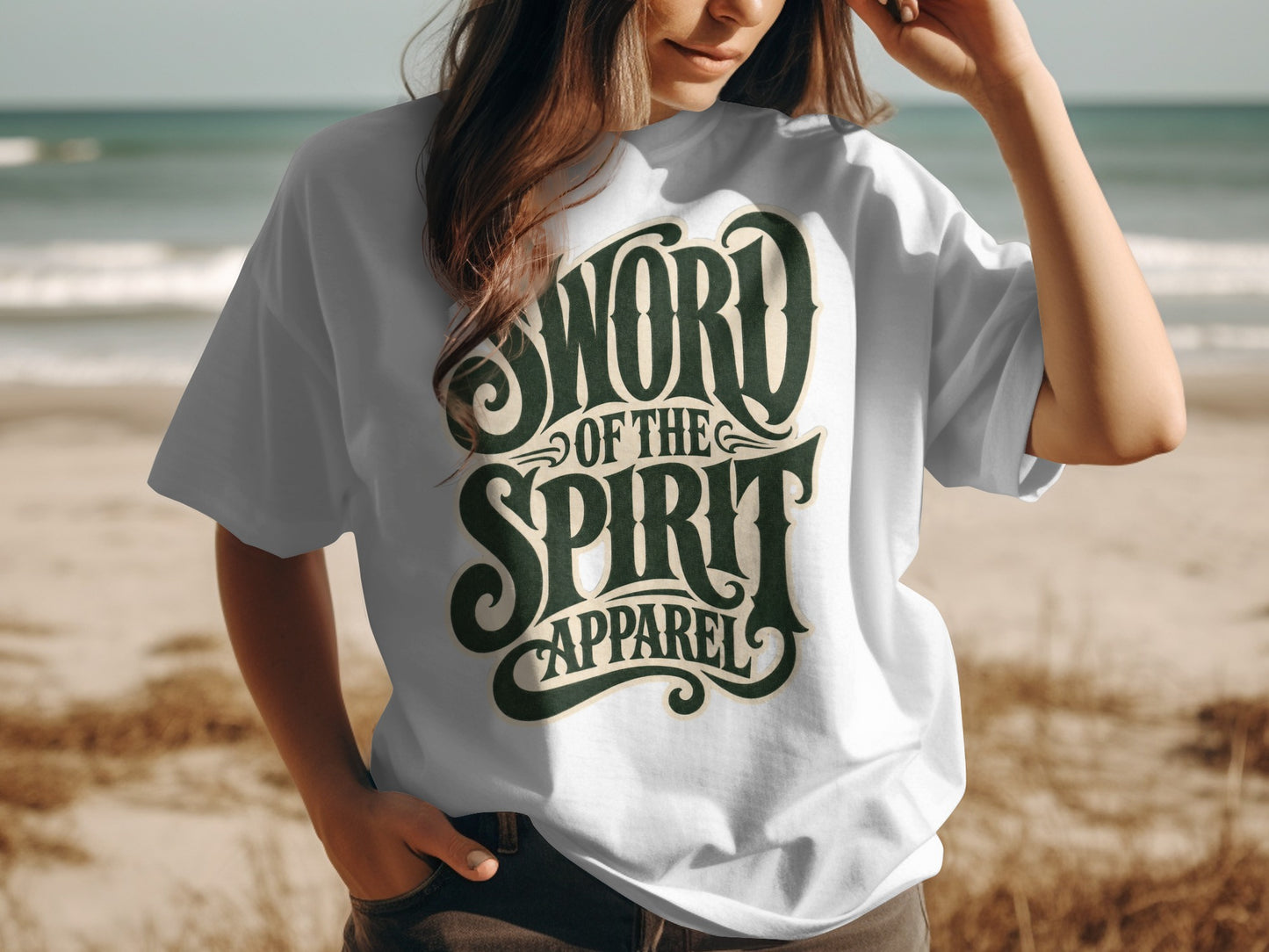 White t-shirt with dark green "SWORD OF THE SPIRIT APPAREL" text on beach background.