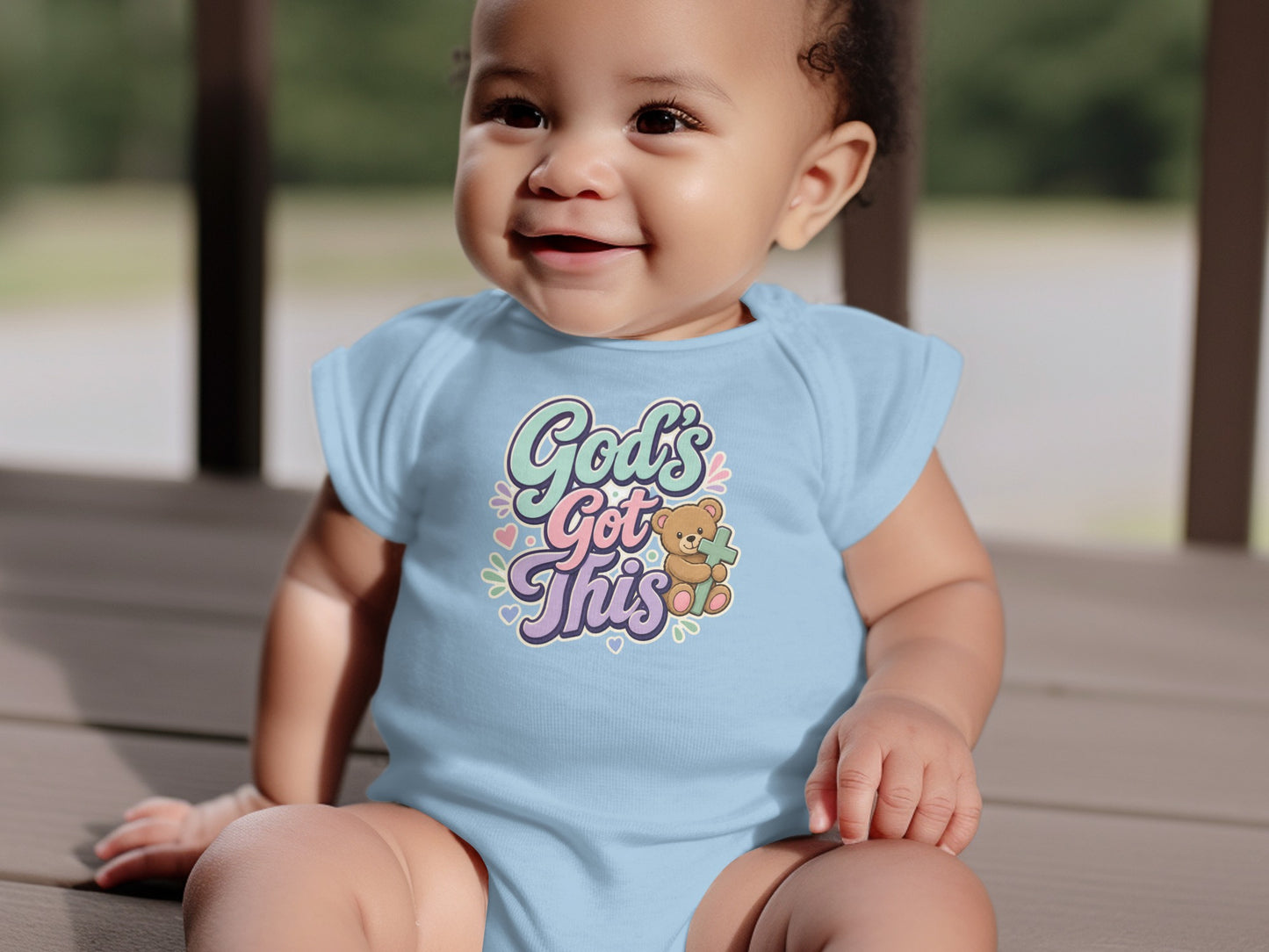 Baby wearing light blue bodysuit with "God's Got This" and a teddy bear.