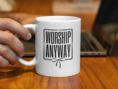 White mug with black text reading "WORSHIP ANYWAY" and a bow design.