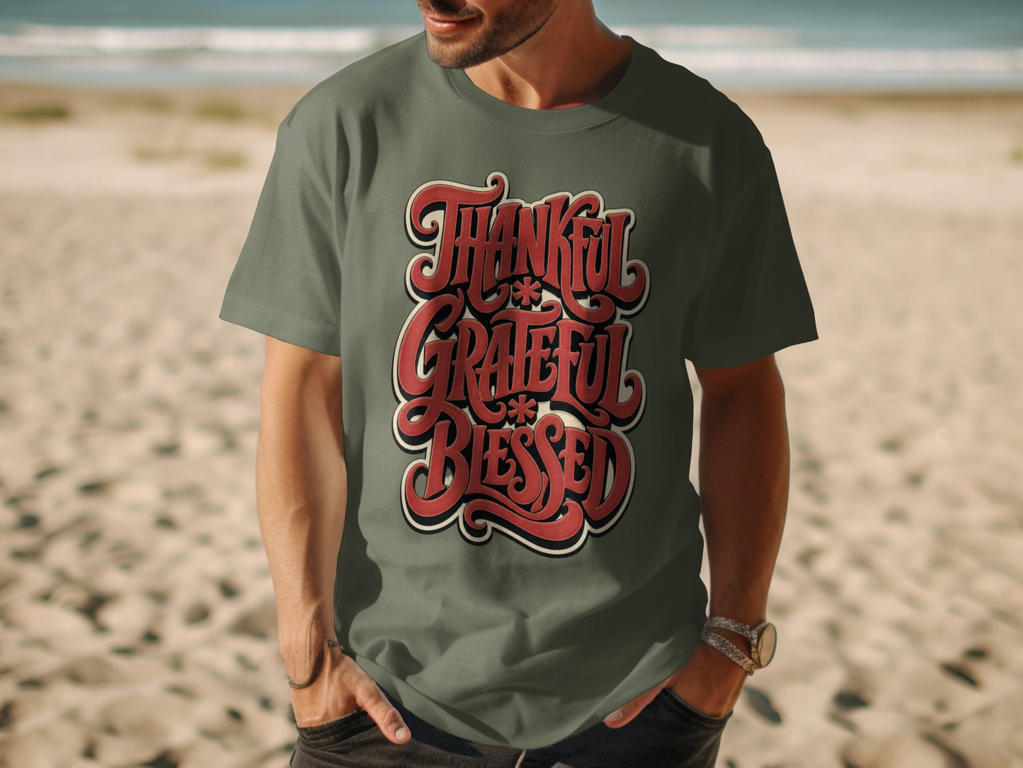 Olive green t-shirt with red text "Thankful Grateful Blessed" on a beach.