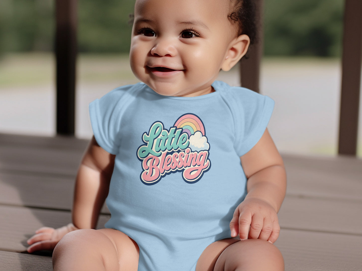 Baby in light blue onesie with "Little Blessing" text and rainbow graphic.