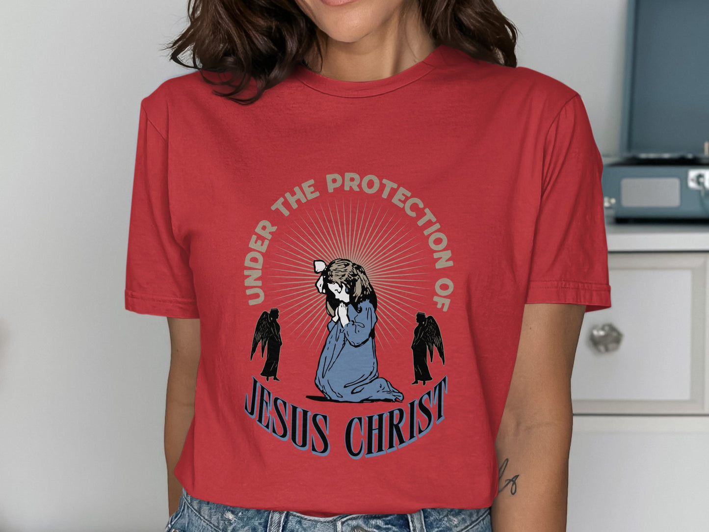 Red t-shirt with "Under the Protection of Jesus Christ" text and praying figure with angels.
