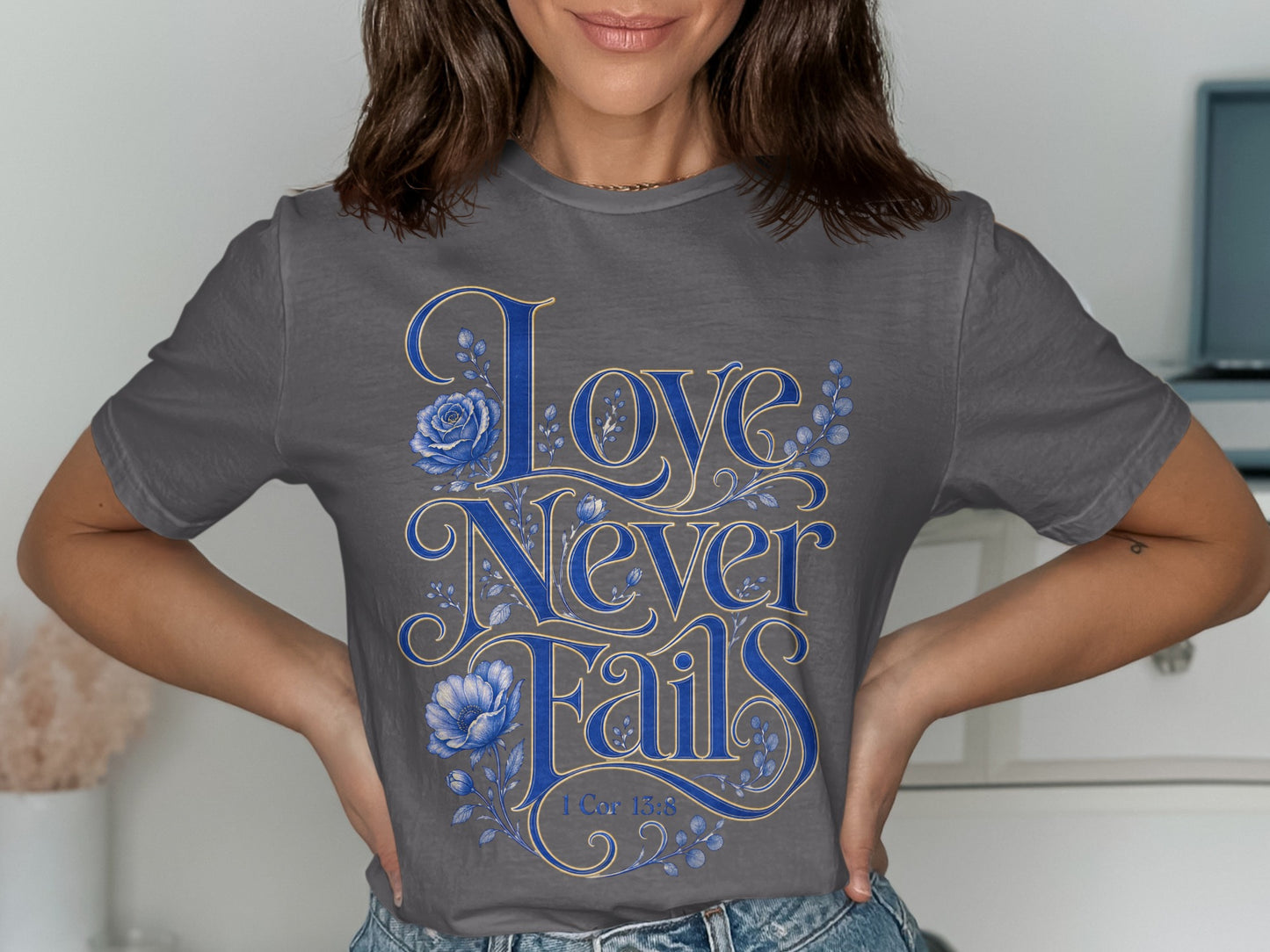 Grey t-shirt with blue script text "Love Never Fails" and floral accents.