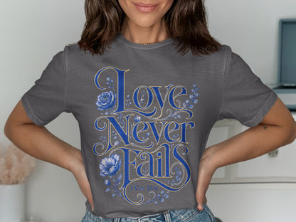 Grey t-shirt with blue script text "Love Never Fails" and floral accents.