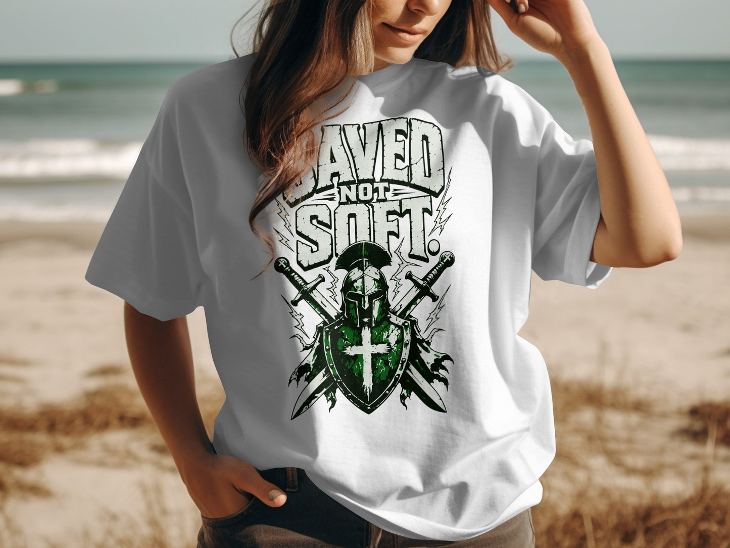 White t-shirt with "Saved Not Soft" text and knight's helmet, shield, and swords graphic.