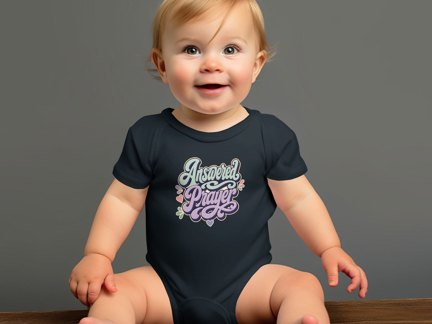 Baby wearing a navy bodysuit with "Answered Prayer" text and floral accents.
