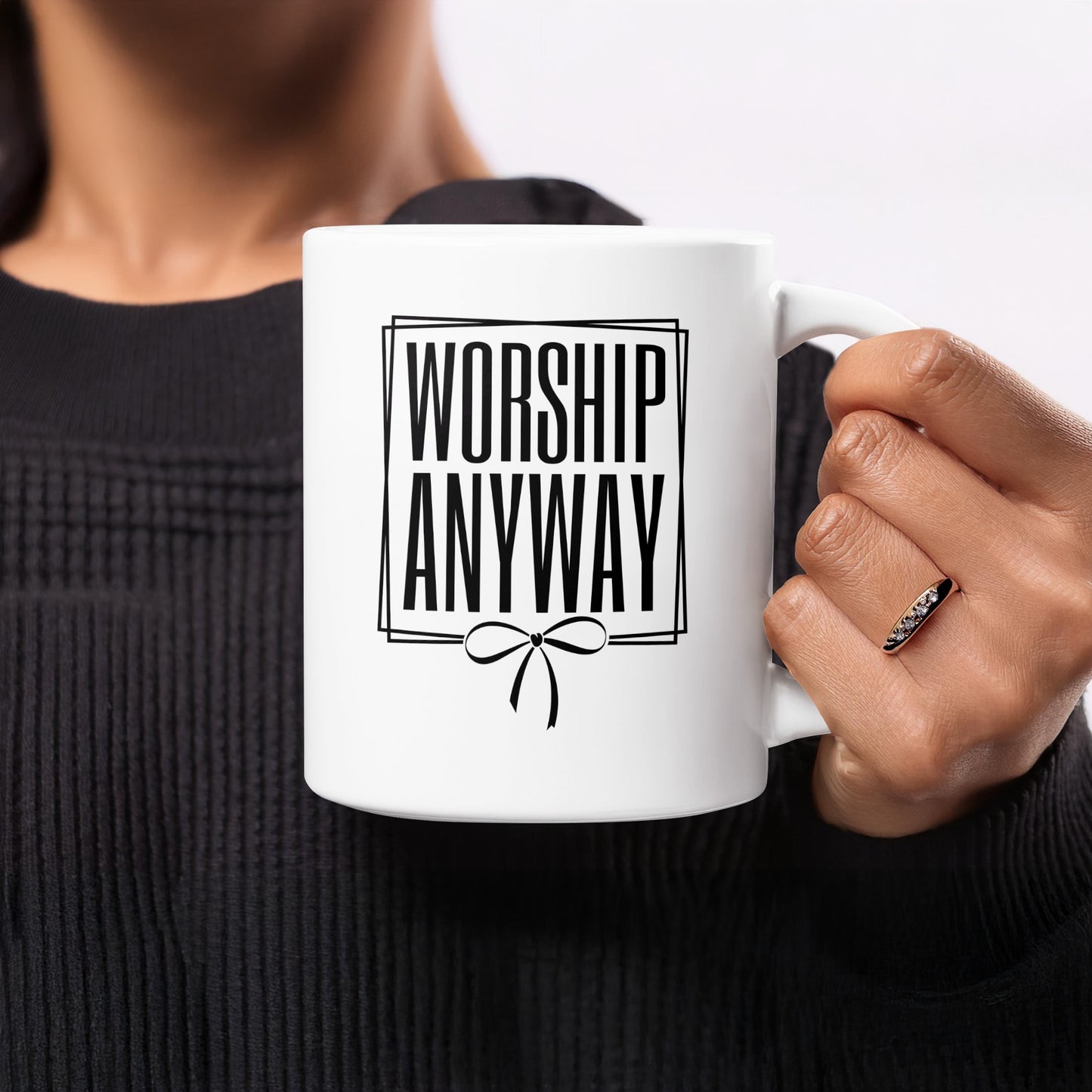 White mug with "WORSHIP ANYWAY" in bold black text and a bow design.