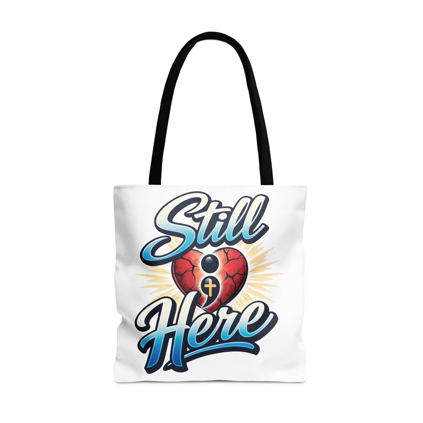 White tote bag with "Still Here" text and a cracked heart with a semicolon and cross.