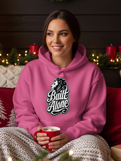 Pink hoodie with "Built Alone" text and lion logo, held by a woman with a mug.
