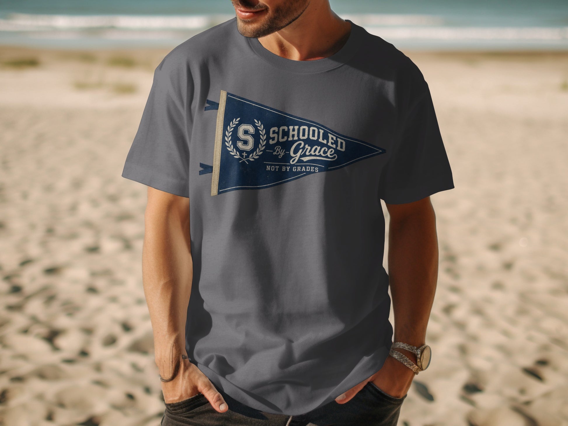 Gray t-shirt with a navy blue pennant graphic reading "Schooled By Grace Not By Grades."